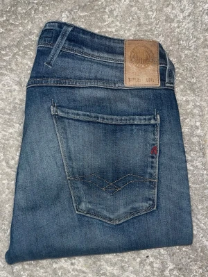 Replay Anbass jeans  - Snygga blå slim fit jeans från Replay med klassisk femficksmodell och diskreta slitningar. Jeansen har en läderpatch med Replay-logga bak i midjan och kontrastsömmar på bakfickan. Tillverkade i mjuk denim för en bekväm känsla.Längd storleken saknas men bedömd till L34 men skulle även kunna vara långa L32. JAG SKICKAR EJ FLER BILDER PÅ JEANSEN! för storleksguide hänvisar jag till måtten och för bättre inblick i passformen rekommenderar jag att googla på modellnamnet. :) 1,101