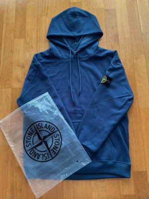 Blå Stone Island hoodie - Helt ny blå Stone Island hoodie i storlek XL. Insidan är täckt i velvet material, extremt skönt 👌.Inga skador eller missfärgningar. Tag sitter kvar. Skriv vid frågor eller funderingar. Pris går att förhandla. Skickar snabbt 📦🚚💨