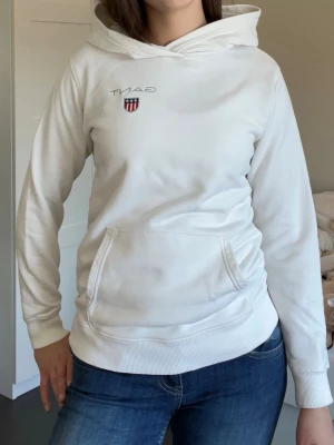 Vit hoodie från Gant - Säljer en vit hoodie från Gant med klassisk huva och magficka. På bröstet finns Gant-loggan. 