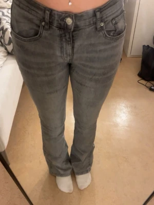 Grå bootcut jeans med låg midja - Säljer ett par grå jeans med bootcut-modell och låg midja. Jeansen har ett par mörka detaljer på olika ställen på byxorna. Använda några gånger