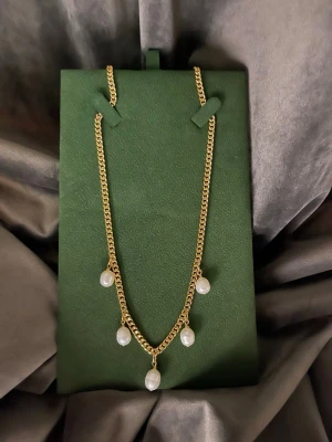 Guldhalsband med pärlhängen - Snyggt halsband i guldpläterad i rostfritt stål  med fem vita pärlhängen som ger en elegant touch. Kedjan har en klassisk design och justerbar längd för perfekt passform. Perfekt accessoar för att lyfta din outfit med lite extra stil.