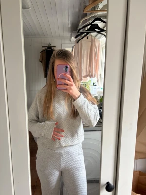 Grått quiltat loungewear-set - Mysigt loungewear-set i ljusgrått med quiltat mönster. Setet består av en långärmad tröja och matchande byxor med mjuk resår i midjan. Perfekt för chill dagar hemma. Materialet känns mjukt och stretchigt, vilket gör det superbekvämt.