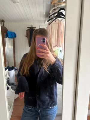 Mörkblå stickad kofta med knappar - Mysig mörkblå stickad kofta med stora knappar framtill och ribbade muddar vid ärmslut och nederkant. Koftan har en avslappnad passform och är perfekt att slänga på sig över en t-shirt. Passar till jeans för en chill look.