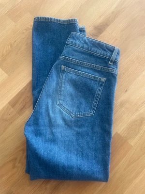 Blå raka jeans från Filippa K - Stella mid blue wash från Filippa K. Croppade, snygga jeans med klassisk femficksmodell och raka ben. Jeansen har en mellanblå tvätt med subtila slitningar och är tillverkade i ett mjukt denimtyg. Storlek 27.