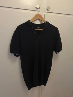 Mörkblå stickad piké  - Snygg mörkblå stickad piké från massimo dutti med korta ärmar och krage med knappar. Perfekt för dig som gillar klassisk och stilren design. Materialet känns mjukt och bekvämt mot huden. Det står L i tröjan men passar mer M-S