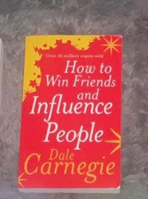 How to Win Friends and Influence People - En klassisk bok av Dale Carnegie med röd och gul mjukpärm. Omslaget har vita och gula texter och stjärnliknande detaljer. Perfekt för dig som vill utveckla dina sociala färdigheter och lära dig mer om personlig utveckling.