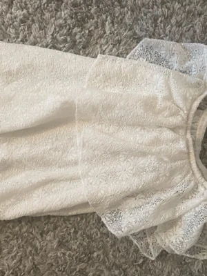 Vit spetsblus med volang - Söt vit blus i spets med blommigt mönster och volangdetaljer vid axlarna. Blusen har rund halsringning och är ärmlös, perfekt för en fräsch och somrig look. Materialet känns lätt och luftigt. Pris kan såklart diskuteras!💕