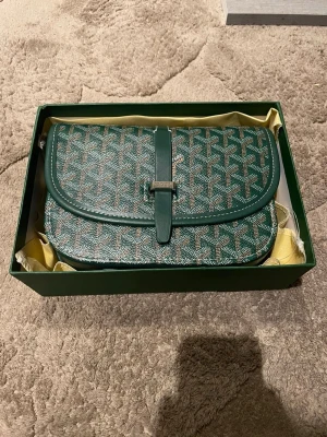 Grön axelväska - Snygg grön axelväska med deras ikoniska mönster i vitt och brunt/grönt. Väskan har en rundad form, lock med spänne och detaljer i svart läder. Perfekt för dig som gillar exklusiva accessoarer och vill sticka ut med en klassisk design. Har i grön färg också båda kommer med packet och dustbag 