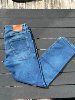 Blå jeans från Jack & Jones - Snygga blå jeans från Jack & Jones i klassisk rak modell. Jeansen har fem fickor, bälteshällor och en läderpatch med logga bak i midjan. Tillverkade i ett mjukt denimtyg som passar perfekt till en avslappnad stil.