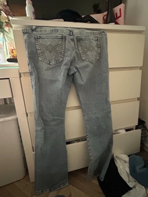 Ljusblå bootcut jeans med broderi - Säljer ett par ljusblå bootcut jeans med snyggt broderi på bakfickorna. Klassisk femficksmodell i mjukt denimtyg. Perfekta för dig som gillar en avslappnad men trendig look.