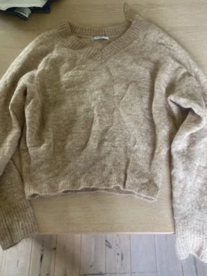 Beige stickad tröja i alpackablandning - Mysig beige stickad tröja från C i alpackablandning. Tröjan har v-ringning, långa ärmar och ribbade muddar vid hals, ärmslut och nederkant. Perfekt för lager på lager och ger en avslappnad men ändå stilren look.