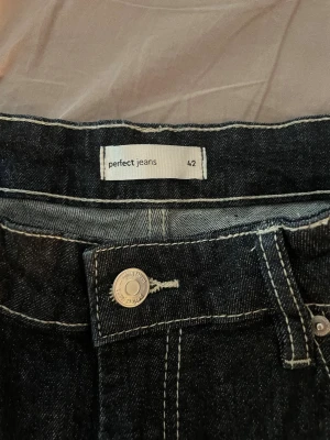 Mörkblå jeans från Perfect Jeans - Säljer ett par mörkblå jeans från Perfect Jeans i storlek 42. Klassisk femficksmodell med kontrastsömmar och silverfärgad knapp. 