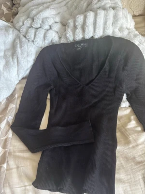 Ribbad tröja  - Svart ribbad topp från Amisu med v-ringning och lång ärm. Sitter tight och har en stretchig passform som framhäver figuren. Perfekt att styla med jeans eller kjol för en clean look.