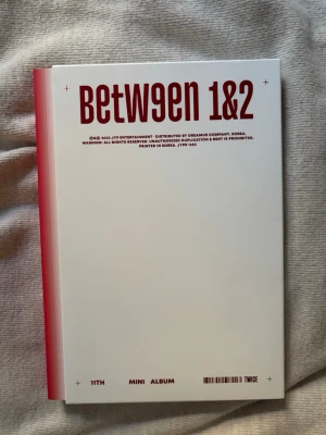 TWICE Between 1&2 Mini Album - TWICE Between 1&2 Mini Album med vitt omslag och röd text. Albumet har en rosa rygg och låtlista på baksidan. Perfekt för dig som gillar K-pop. Alla photocards och sådant finns med i albumet, cd:et är inte skadat. Den är som ny!