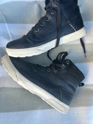 Svarta kängor från Björn Borg - Säljer ett par svarta kängor från Björn Borg med högt skaft och snörning. Skorna har en vit, rejäl sula och är tillverkade i läder med detaljer i mocka vid ankeln. Perfekta för dig som vill ha en stilren och bekväm sko till vardags. Dessutom knappt använd så luktar som ny 