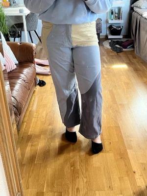 Patchwork jeans i beige och grå - Unika patchwork jeans med beige och olika nyanser av grått. Vida ben och hög midja ger en avslappnad vibe. Snygga kontrastsömmar och flera fickor framtill. Perfekta för dig som vill sticka ut med en cool och trendig look.