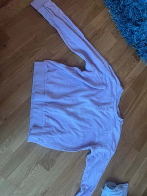 Ljuslila sweatshirt med rund hals - En enkel och stilren ljuslila sweatshirt med rund halsringning och långa ärmar. Tröjan har breda muddar vid ärmslut och nederkant för en avslappnad look. Perfekt att matcha med jeans eller mjukisbyxor.