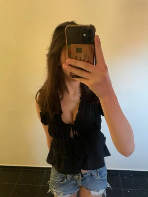 Svart volangblus med knyt från Gina Tricot - Supersöt svart blus från Gina Tricot med volangdetaljer och knyt framtill!