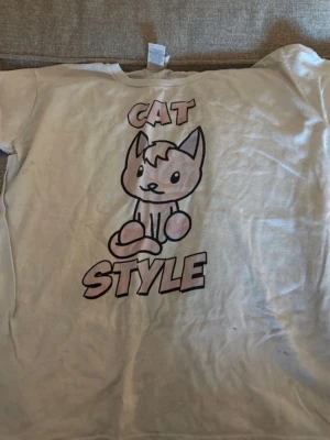 Vit Cat Style t-shirt med kattmotiv - Cool vit t-shirt med ett stort tryck av en söt tecknad katt och texten 'CAT STYLE' på framsidan. Perfekt för dig som gillar unika och lekfulla prints. T-shirten har rund hals och korta ärmar, och är gjord i mjuk bomull.
