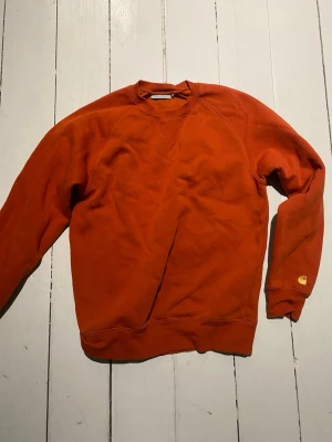 Rostfärgad sweatshirt från Carhartt - Säljer en rostfärgad sweatshirt från Carhartt Work In Progress. Tröjan har rund halsringning, ribbade muddar och en liten Carhartt-logga på ärmen. Tillverkad i mjuk bomullsblandning och har en avslappnad passform.