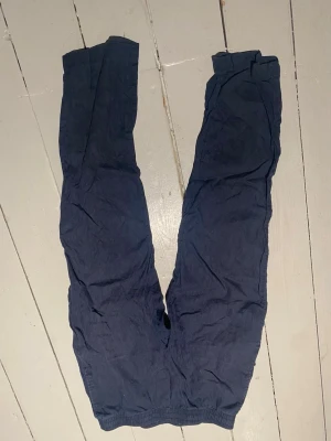 Mörkblå mjukisbyxor med resår - Säljer ett par mörkblå mjukisbyxor med resår i midjan. Byxorna har en enkel och avslappnad passform, perfekta för chill dagar hemma eller när du vill vara bekväm. Tillverkade i ett mjukt och lätt material som känns skönt mot huden.