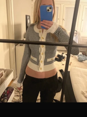 Randig kofta från Hope & Bille - Säljer en snygg, söt kofta . Koftan är vit med svarta smala ränder, har guldfärgade knappar och dekorativa fickor framtill. Långa ärmar och ribbade muddar ger en trendig look. Perfekt för dig som gillar en mer classy stil , (den är aldrig använd med lappen kvar) 