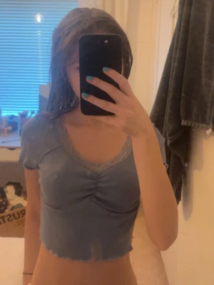 Blå croppad topp med spetskant - Söt ljusblå croppad topp med v-ringning och spetskant runt halsen. Toppen har korta ärmar och rynkdetalj framtill som ger en snygg form. Perfekt till jeans eller kjol för en trendig look. Passar perfekt nu till sommaren. Men lapp saknas och vet därför inte storlek eller varumärke. Men jag bör oftas Xs.