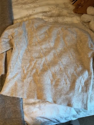 Beige kabelstickad tröja Gina Tricot - Mysig beige kabelstickad tröja från Gina Tricot. Tröjan har ett klassiskt flätmönster, ribbade muddar och rund hals. Perfekt för kalla dagar och enkel att matcha med jeans eller kjol.