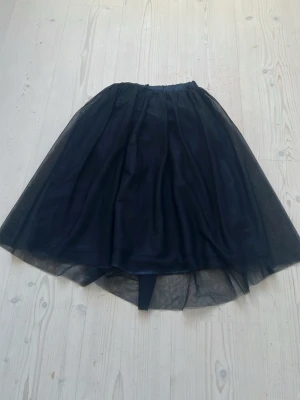 Svart tyllkjol från Name It - Säljer en svart tyllkjol från Name It med elastisk midja. Kjolen har flera lager tyg som ger en voluminös och luftig känsla. Perfekt för dig som vill ha en klassisk och stilren look med lite extra volym.