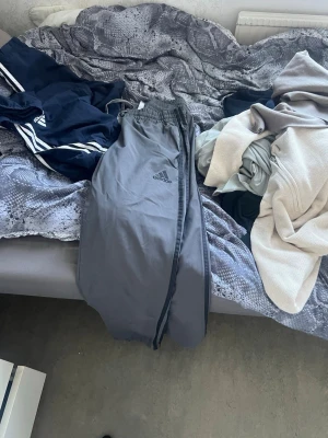 Grå Adidas mjukisbyxor - Snygga grå mjukisbyxor från Adidas med klassisk logga på benet. Byxorna har avslappnad passform och resår i midjan. Perfekta för chill eller träning. Materialet är mjukt och bekvämt.