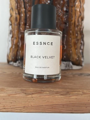 Essnce Black Velvet Eau de Parfum - En stilren parfym från Essnce med namnet Black Velvet. Flaskan är cylindrisk i klart glas med svart lock och etikett i minimalistisk design. Innehållet har en djup bärnstensfärg som ger en lyxig känsla. Perfekt för dig som gillar eleganta och moderna dofter.