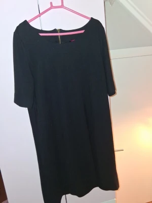 Svart enkel klänning med halvärm - Svart klänning med rund halsringning och halvärm. Klänningen har en rak passform och dragkedja i ryggen. Perfekt för dig som gillar en stilren och minimalistisk look.