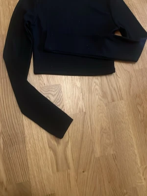 Svart croppad långärmad topp - En svart, croppad långärmad topp med enkel och stilren design. Toppen har en tight passform och är tillverkad i ett stretchigt material som sitter snyggt på kroppen. Perfekt att matcha med höga jeans eller kjol.