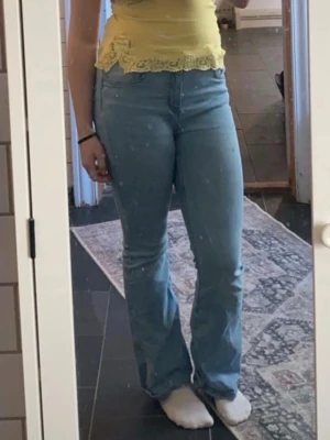 Ljusblå bootcut jeans - Säljer ett par ljusblå bootcut jeans med hög midja och klassisk femficksdesign. Jeansen har en snygg utsvängd passform nertill och är tillverkade i denim. Perfekta för dig som gillar en retroinspirerad stil. Flare/bootcut modell i ljusblått. Hög/mid midja.  Regular längd. Säljer då jag har två par och bara behöver ett. 