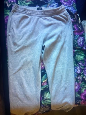 Grå mjukisbyxor från H&M - Säljer ett par klassiska grå mjukisbyxor från H&M med resår i midjan och benslut. Byxorna har två sidofickor fram och en bakficka. Perfekta för chill dagar hemma eller när du vill ha det extra bekvämt. Tillverkade i mjukt sweatshirtmaterial.