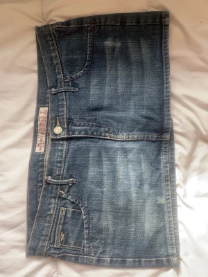 Jeanskjol från Hollister - Snygg blå jeanskjol från Hollister med klassisk femficksdesign och slitna detaljer. Kjolen har en kort modell och är tillverkad i bomull med en cool tvättad look. Perfekt för dig som gillar en avslappnad och trendig stil.