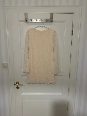 Ljus spetsklänning med lång ärm - Söt ljus kortklänning med transparenta långärmar och vackert spetsmönster. Klänningen har en rak passform och är täckt av små broderade detaljer som ger en romantisk känsla. Perfekt för dig som gillar en feminin och stilren look. Står storlek M men jag skulle säga ish xs/s. Bara testat en gång. 