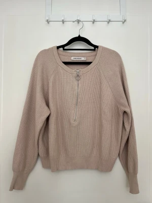 Beige stickad tröja med dragkedja - Snygg beige stickad tröja från Carin Wester med halv dragkedja framtill och rund halsringning. Tröjan har långa ärmar, ribbstickade muddar och är gjord i ett mjukt material.