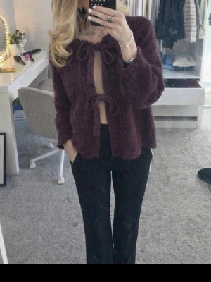 Stickad lila kofta med knyt - Mysig stickad kofta i mörklila med långa ärmar och två rosettknyt framtill. Cardigan har en loose passform och är perfekt för lager-på-lager-stil. Enkel men trendig design som passar till många outfits.