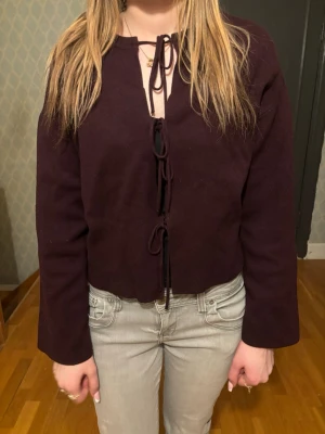 Mörklila kofta med knytning fram - Snygg mörklila kofta med knytning framtill och rak passform. Koftan har långa ärmar och är tillverkad i ett mjukt stickat material. Perfekt för lager-på-lager och ger en chill vibe till din outfit.