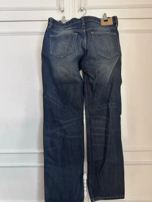 Mörkblå raka jeans med medel hög midja - Snygga mörkblå jeans med raka ben och klassisk femficksdesign. Jeansen har hög midja och subtila slitningar framtill för en cool look. Tillverkade i denim med kontrastsömmar. Perfekta för dig som gillar en avslappnad och tidlös stil.