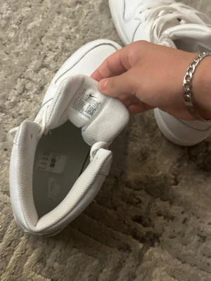 Vita Nike high top sneakers - Säljer ett par helvita Nike sneakers med högt skaft och klassisk swoosh på sidan. Skorna har snörning och är tillverkade i slätt läder med meshdetaljer vid plösen. Perfekta för dig som gillar en clean och sportig stil.
