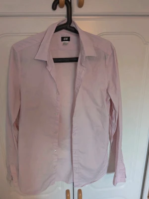 Ljusrosa skjorta från H&M, strl S - Klassisk ljusrosa skjorta från H&M i storlek S. Skjortan har lång ärm, knappar framtill och en tidlös krage. Tillverkad i bomull för en skön och lätt känsla. Perfekt för en clean och enkel stil.