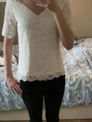 Vit spetsblus med v-ringning - Snygg vit blus i spets med v-ringad hals och halvkort ärm. Blusen har fina spetsdetaljer. Fråga om du vill ha mera bilder 