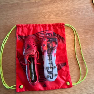 Röda Adidas Fotbollsskor Predator - Säljer nu ett par riktigt feta röda Adidas fotbollsskor med vita och svarta detaljer. Skorna har snörning och rund tå, samt konstgräsdobbar under sulan för bra grepp på planen. Perfekta för dig som vill sticka ut på fotbollsplanen! Säljer endast då skorna var för stora och det är för sent att lämna tillbaka dem. Nypris ligger runt 3500 kr. Skorna är använda cirka 5 gånger och är i otroligt bra skick - men lite smutsiga. Priset är inte hugget i sten - kontakta vid minsta fundering.