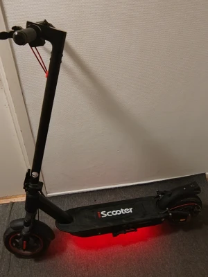 Svart elscooter från iScooter - Elektrisk scooter från iScooter i svart färg med röda detaljer och LED-belysning under. Scootern har robust ram, stora hjul och handtag med greppvänligt material. Perfekt för att ta sig runt snabbt och smidigt i stan. Och det kommer med kartongen .