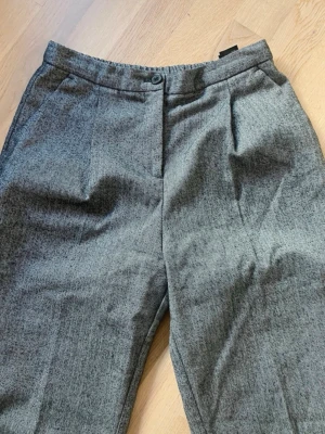 Grå kostymbyxor - Grå kostymbyxor från Monki i storlek 36. Material: 65% polyester, 35% viskos. Passar bra för att ha på kontoret eller vid andra tillfällen.