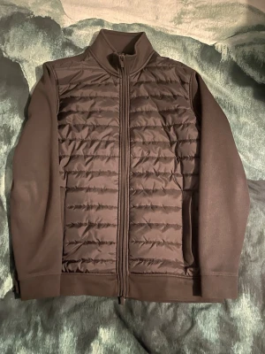 Svart quiltad cardiganjacka Dressmann - Snygg svart cardiganjacka från Dressmann i storlek L. Jackan har quiltad front med dragkedja hela vägen, höga muddar och ståkrage. Ärmar och rygg är i mjukt tyg medan framsidan är vadderad för extra värme. Perfekt för lager på lager och stilren look.