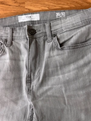 Grå jeans från FSBN, raka ben - Snygga grå jeans från FSBN med klassisk femficksmodell och raka ben. Jeansen har normal midja, bälteshällor och stängs med knapp och dragkedja. Perfekta för en clean och avslappnad stil. Materialet är mjukt och följsamt denim.