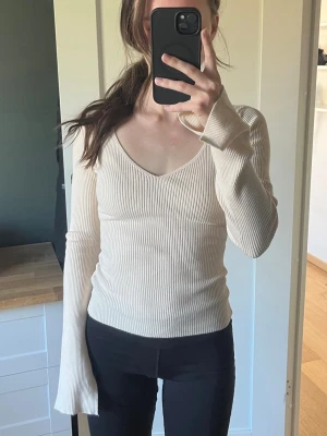 Beige ribbad långärmad topp - Säljer en beige ribbad topp med v-ringning och långa ärmar. Toppen har en slim passform och är tillverkad i ett mjukt material som sitter snyggt på kroppen. Perfekt att matcha med jeans eller kjol för en stilren look.